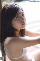 A woman in a white bra and panties leaning against a window.