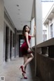 A woman in a red dress leaning against a wall.