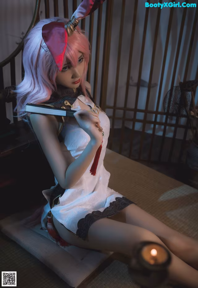 A woman with pink hair sitting on a bed holding a knife.