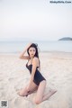 A woman in a black bathing suit sitting on a beach.