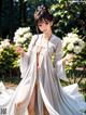 A woman in a white kimono standing in a garden.