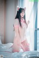A woman in a pink and white outfit sitting on a bed.