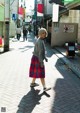 A woman walking down a street in a plaid skirt.