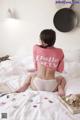 A woman sitting on a bed in a pink sweater and white panties.