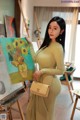 A woman in a yellow dress holding a painting.