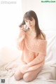 A woman in a pink sweater sitting on a bed.