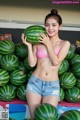 A woman in a pink bikini holding a watermelon.