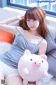 A woman sitting on a bed holding a pink pig pillow.