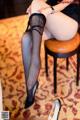 A woman sitting on a stool wearing black stockings and high heels.