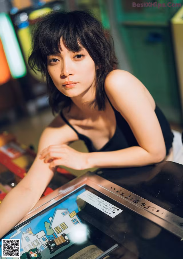 A woman sitting at a table with a pinball machine.